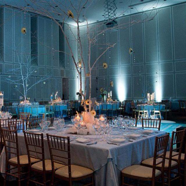 Room with large square tables draped in white with blue uplighting 