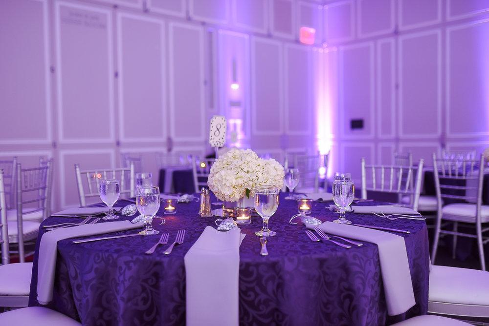 Table dressed with purple linen, white flowers and purple uplighting