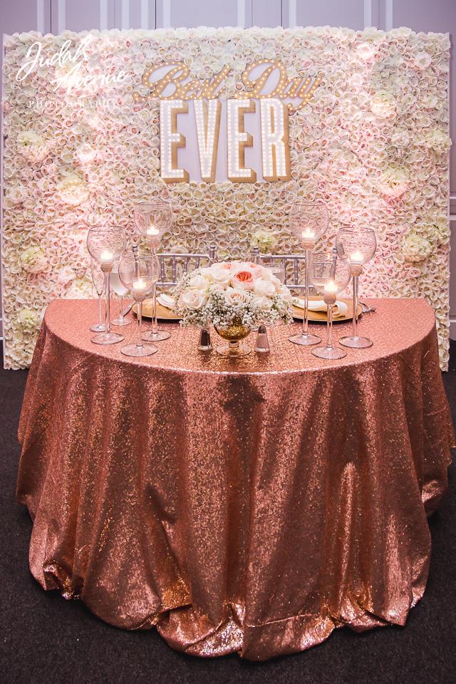 Sweetheart table with shimmering rose gold linen and floral backdrop