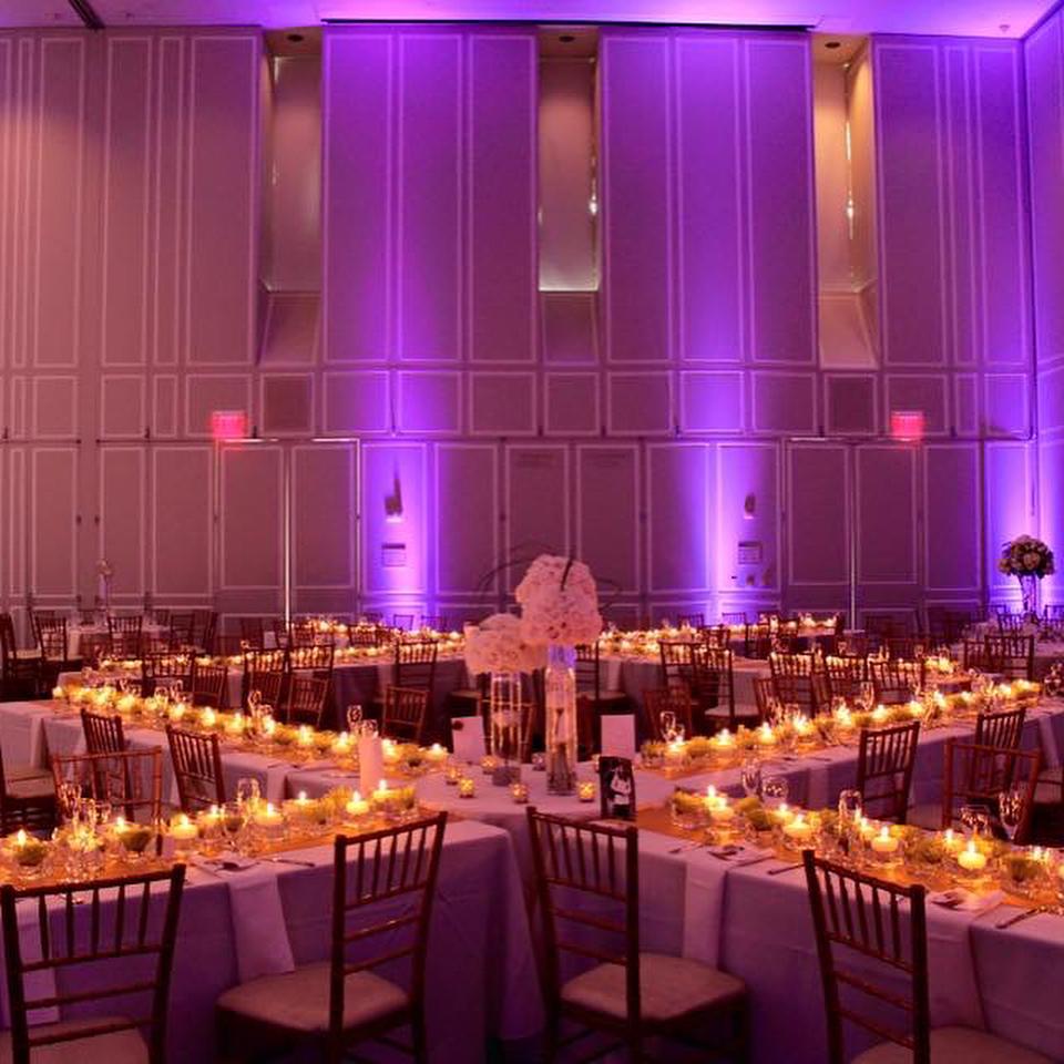 Dramatic X shaped tables set with candles and purple uplighting